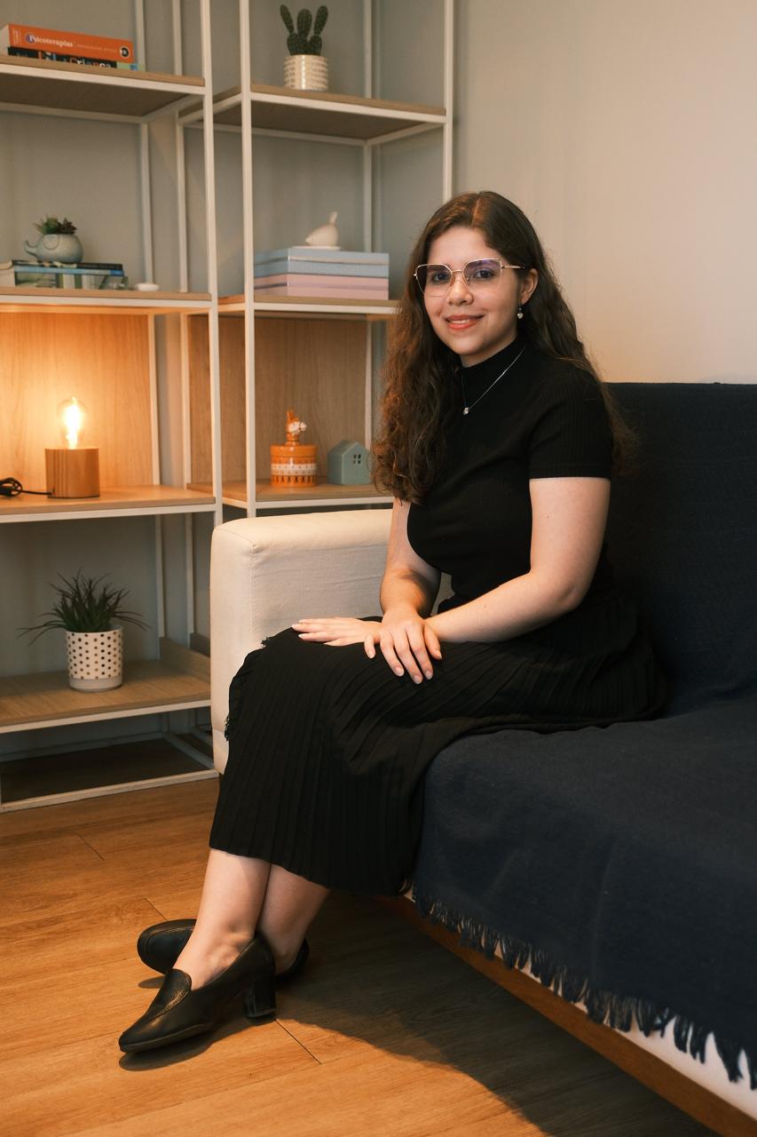 Retrato de Luana Coelho, psicóloga, sentada em seu consultório acolhedor.